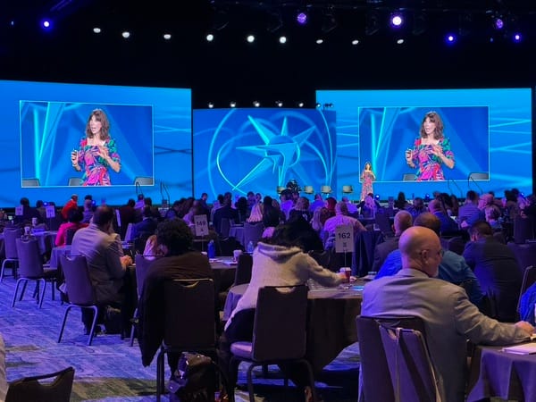 Antoinette Griffin speaking in front of two large TVs